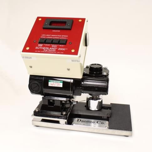The Sutherland Rub Test machine which is a red and white box that sits above computer equipment and samples